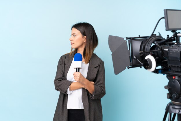 Journaliste femme tenant un microphone et rapportant des nouvelles sur le mur bleu à côté