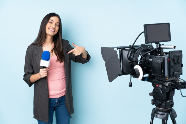 Journaliste femme tenant un microphone et rapportant des nouvelles sur le mur bleu, fière et satisfaite