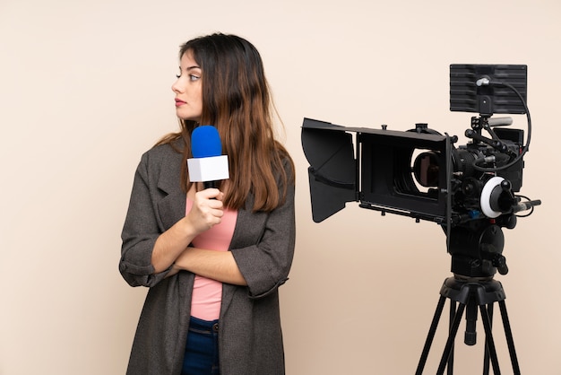 Journaliste femme tenant un microphone et rapportant des nouvelles sur le mur isolé à la recherche de côté