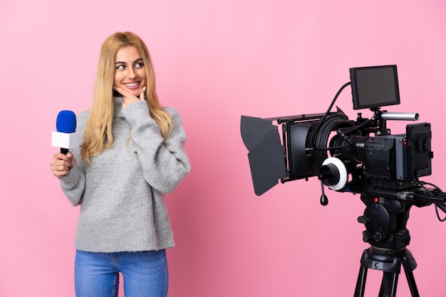 Journaliste femme tenant un microphone et rapportant des nouvelles sur le mur rose à côté et souriant