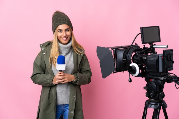 Journaliste femme tenant un microphone et rapportant des nouvelles sur le mur rose isolé en riant