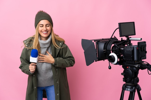 Journaliste femme tenant un microphone et rapportant des nouvelles sur rose isolé souriant beaucoup