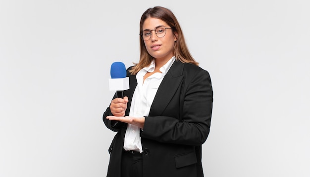 Journaliste de jeune femme souriant joyeusement, se sentant heureux et montrant un concept dans l'espace de copie avec la paume de la main