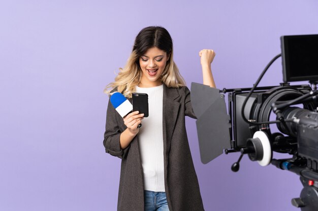 Journaliste jeune femme tenant un microphone et rapportant des nouvelles isolées sur un mur violet surpris et envoyant un message