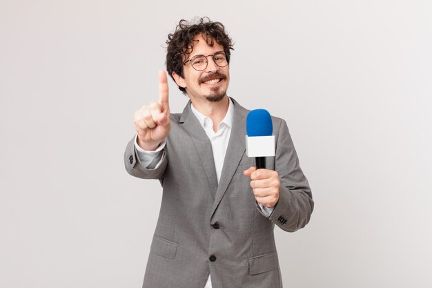 Journaliste de jeune homme souriant fièrement et avec confiance faisant le numéro un