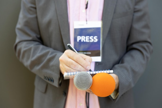 Photo journaliste lors d'une conférence de presse ou d'un événement médiatique écrivant des notes en tenant un microphone