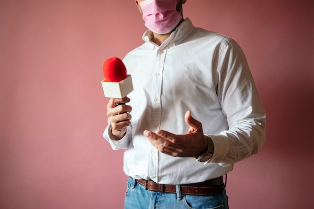 Photo journaliste portant un masque avec microphone debout avec fond rose