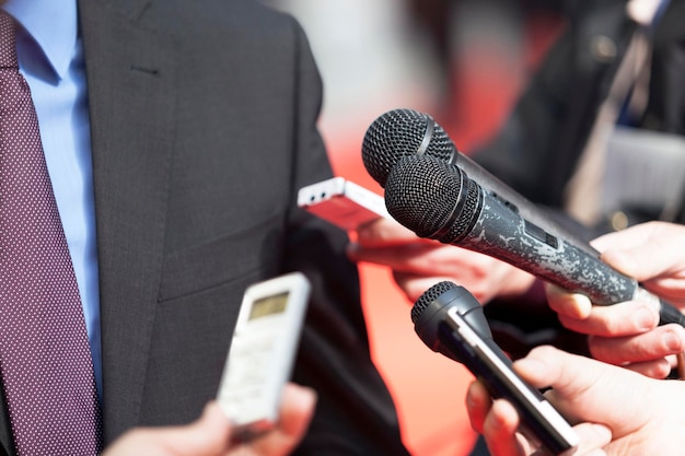 Photo des journalistes tenant des microphones devant un homme d'affaires.