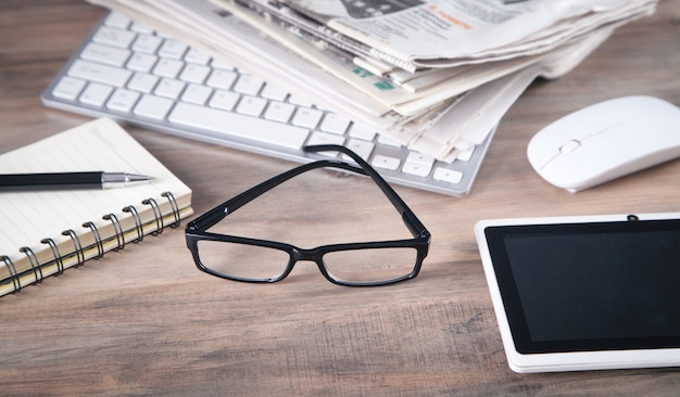 Journaux, clavier d'ordinateur, lunettes sur la table en bois.