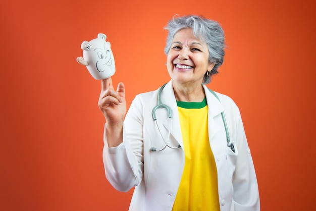 Journée du pédiatre Femme médecin mature aux cheveux gris et jouets pour enfants isolés sur fond orange