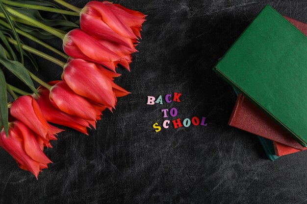 Journée du savoir. Tulipes rouges avec pile de livres sur tableau noir. Vue de dessus. Mot de retour à l'école