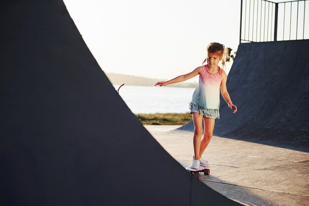 Journée ensoleillée. L'enfant s'amuse avec le patin à la rampe. Joyeuse petite fille.