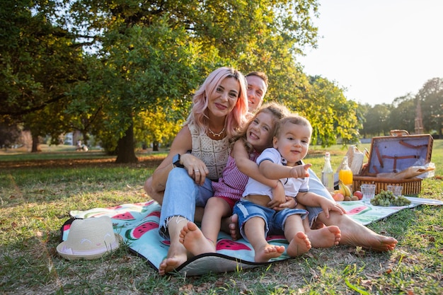 Journée ensoleillée Famille de quatre personnes assises sur un tapis de pique-nique dans le parc ayant un pique-nique végétarien