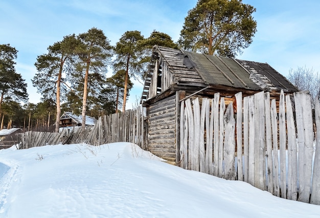 Journée d'hiver au village. Une ancienne grange et une clôture en bois se dresse près de la forêt.