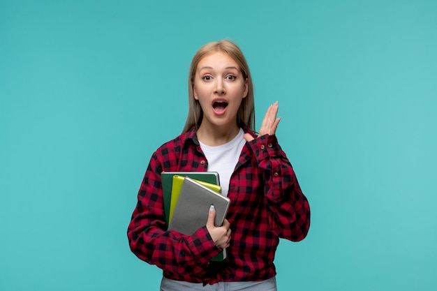 Journée internationale des étudiants jeune fille mignonne en chemise à carreaux rouge choquée avec des livres à la main