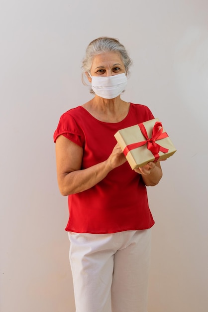 Journée internationale de la femme Femme mature avec masque pandémique tenant un cadeau isolé sur blanc