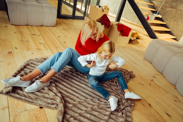 Journée à la maison. Incroyable enfant blond assis sur le sol et s'amusant avec sa mère