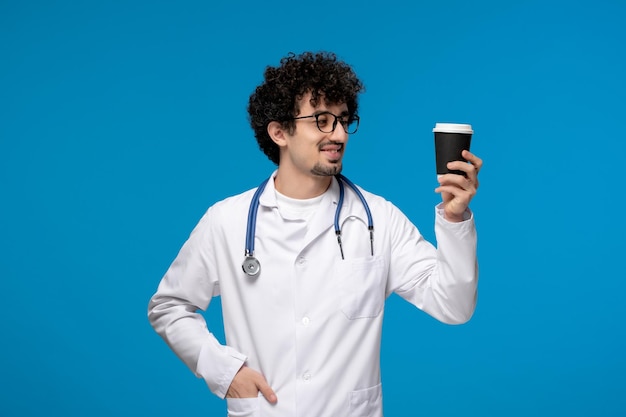 Journée Des Médecins Mec Mignon Brune Bouclée En Blouse De Laboratoire Avec Des Lunettes Tenant Une Tasse De Café