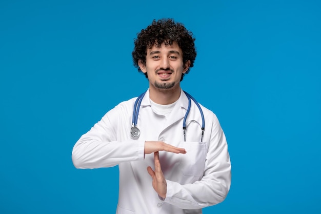 Journée des médecins mec mignon brune bouclée en uniforme médical montrant un panneau d'arrêt et souriant