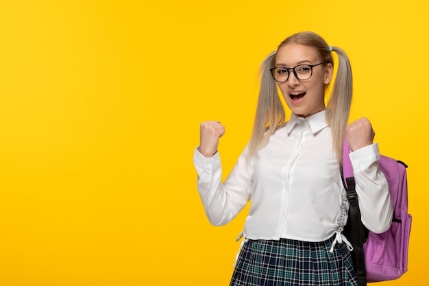 Journée mondiale du livre joyeuse écolière blonde acclamant avec sac à dos sur fond jaune