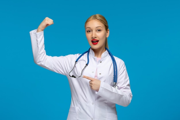 Journée mondiale des médecins médecin mignon fort montrant des biceps avec le stéthoscope dans la blouse médicale