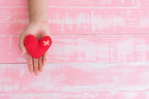 Journée mondiale de la santé, main d&#39;enfant sur coeur rouge à la main sur fond en bois rose