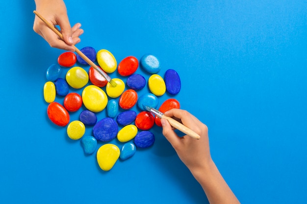 Journée mondiale de sensibilisation à l'autisme. Enfants mains peignant avec des brosses coeur en pierres de couleurs bleu rouge jaune