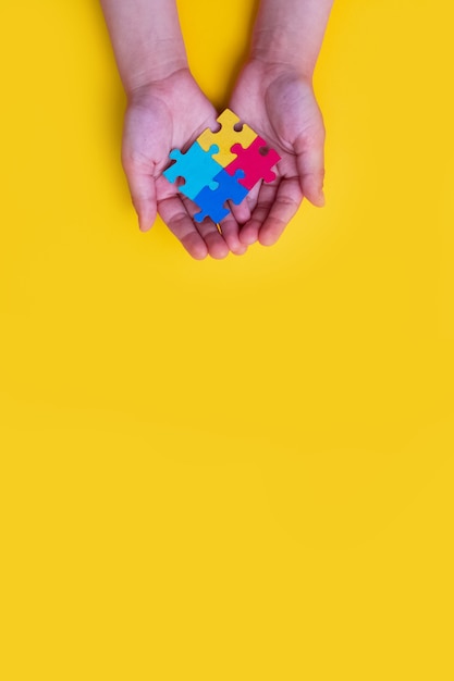 Journée mondiale de sensibilisation à l'autisme Mains de petit enfant tenant des puzzles colorés sur fond jaune