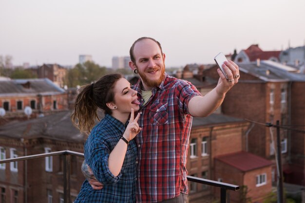 Journée de plaisir sur le toit. Technologie moderne. Jeunes gens heureux prenant un selfie à l'extérieur, temps de loisirs joyeux, jeunes élégants au premier plan, concept de bonheur