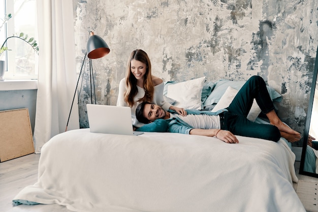 Journée relaxante. Beau jeune couple utilisant un ordinateur tout en passant du temps au lit à la maison