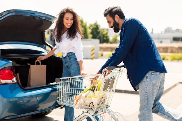 Journée shopping en famille couple arabe mettant des sacs pleins de nourriture fraîche dans la voiture debout à l'extérieur après