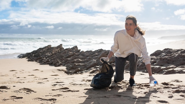 Journée de la terre Femme volontaire avec un sac en polyéthylène ramassant une bouteille en plastique sur le panorama de la plage avec espace libre