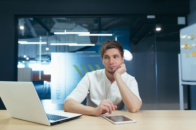 Journée de travail ennuyeuse Portrait d'un jeune homme assis au bureau au bureau triste tenant sa tête dans sa main Il n'aime pas son travail Fatigué