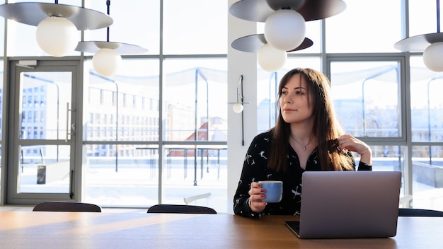 Journée de travail d'un pigiste une jeune femme boit du café et travaille sur un ordinateur portable dans un café Copy Space