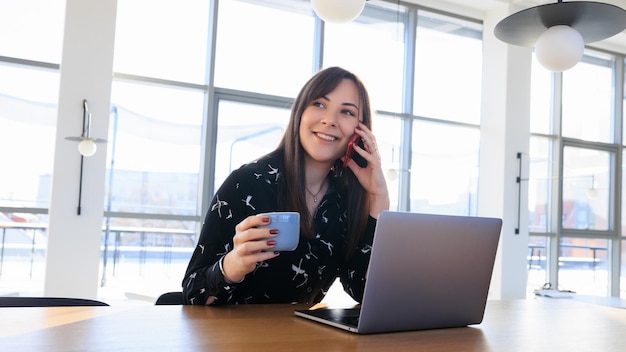 Journée de travail d'un pigiste - une jeune femme parlant au téléphone et buvant du café dans un café