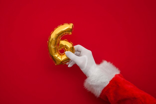 Les jours de Noël, les mains du Père Noël tiennent le ballon du jour sur un fond rouge.