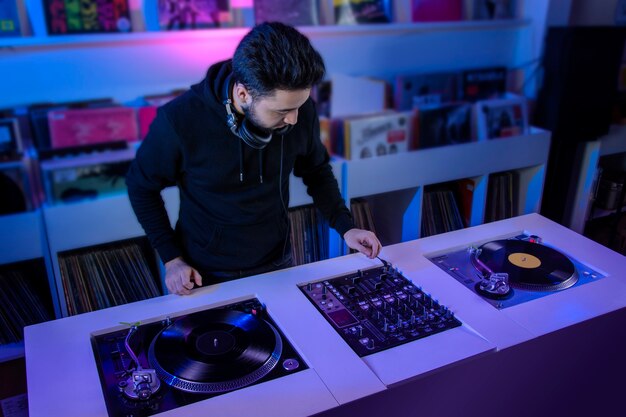 Joven dj mezclando musica en una tienda de discos de vinilo usando un tornamesa de audio