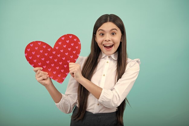 Joyeuse belle adolescente romantique tenir coeur rouge symbole de l'amour pour la Saint Valentin isolé sur fond bleu