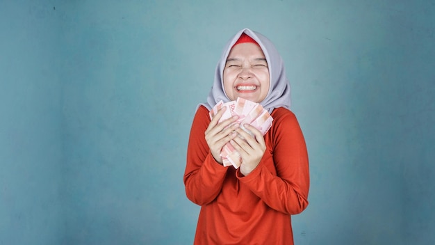 Joyeuse belle femme asiatique dans une chemise décontractée et un hijab montrant des billets en roupies indonésiennes