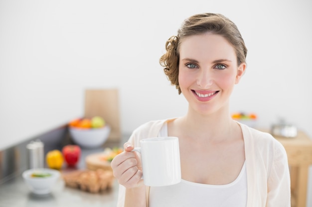 Joyeuse belle femme debout dans sa cuisine tenant une tasse