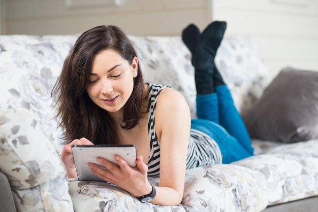 Joyeuse belle jeune étudiante aime la tablette sur le canapé dans la chambre à la maison