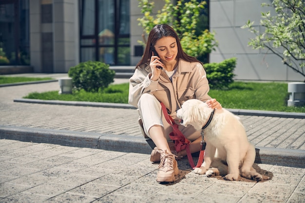 Joyeuse belle jeune femme assise sur le bord du trottoir à côté de son chien