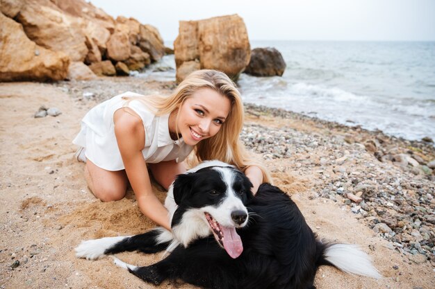 Joyeuse belle jeune femme serrant son chien sur la plage