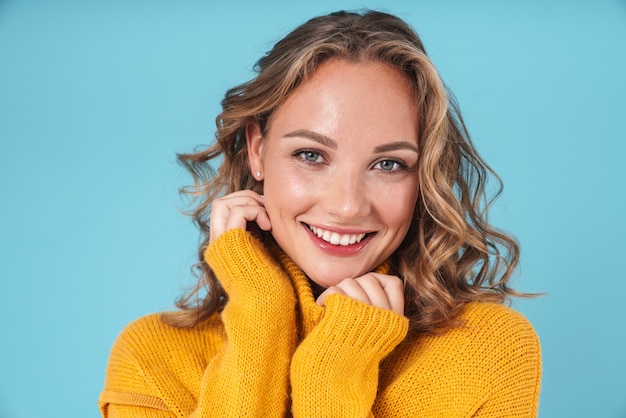 Joyeuse belle jeune fille portant un chandail debout isolé sur bleu