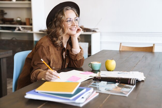 joyeuse charmante femme à lunettes souriant tout en étudiant avec des cahiers à la maison