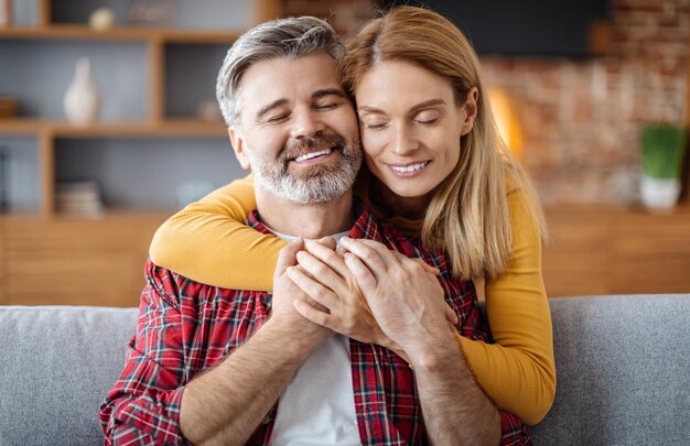 Joyeuse dame caucasienne d'âge moyen étreignant son homme profitez d'un moment tendre avec les yeux fermés pendant le temps libre