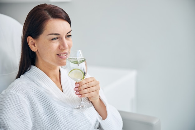 joyeuse dame caucasienne dans un peignoir buvant de l'eau infusée à la chaux et à la menthe