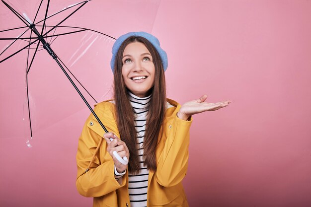 Photo joyeuse dame en chemisier à rayures et veste de pluie jaune tient la main de côté comme s'il pleuvait