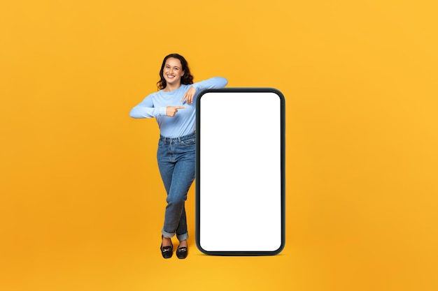 Une joyeuse dame du millénaire montrant un énorme téléphone avec un écran vierge