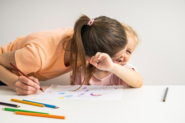 Joyeuse étreinte maman et enfant fille dessinent ensemble avec des crayons de couleur sur papier